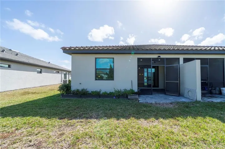 Rear exterior featuring a tile roof, screened-in patio, and paved hardscaping