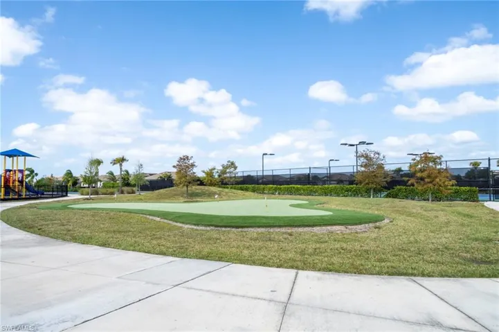 Putting green with synthetic turf, concrete walking path, fenced tennis court, and playground equipment