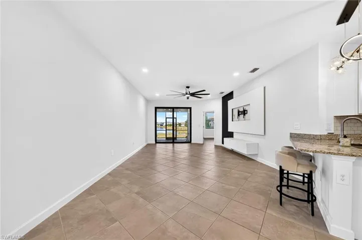 Open-concept interior featuring large-format diagonal tile flooring, recessed lighting, ceiling fan, built-in media wall cabinetry, and glass sliding doors