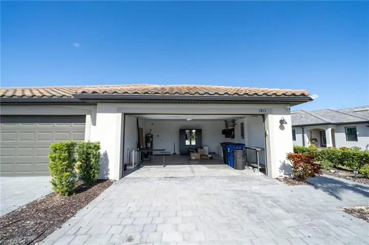 Stucco exterior featuring a dual-bay garage with a paver driveway, tile roofing, and integrated wall-mounted lighting