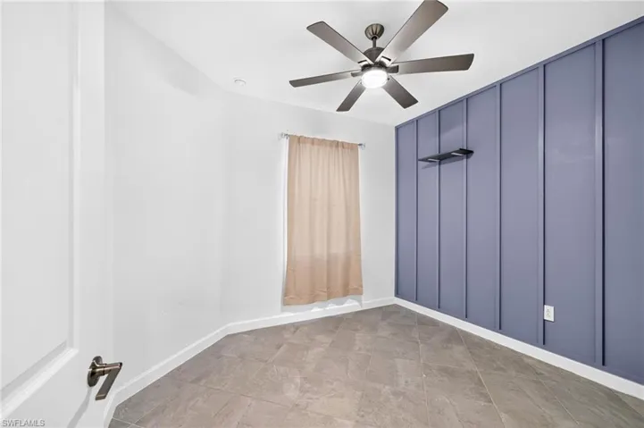 Room featuring a blue board-and-batten accent wall, tile flooring, and a multi-blade ceiling fan with integrated lighting