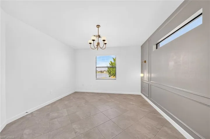 Interior room featuring tile flooring, wainscot paneling on a feature wall, a transom window, a secondary window, and a multi-arm chandelier