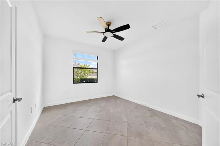 Room featuring neutral-toned tile flooring, white walls, and a multi-blade ceiling fan with integrated lighting