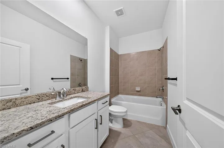 Bathroom featuring white cabinetry, stone-surface countertop with an integrated rectangular sink, wall-spanning mirror, and a tub-shower combination with tiled surround