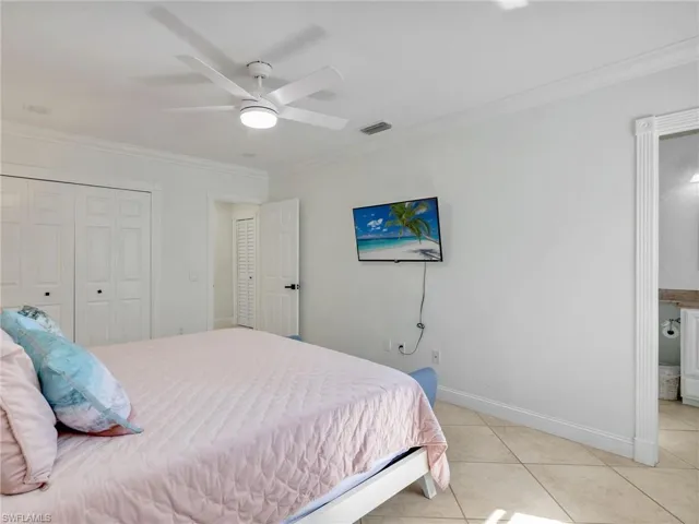 Bedroom featuring crown molding, light tile patterned flooring, ceiling fan, a closet, and ensuite bath