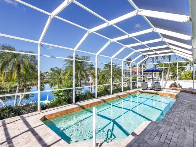 Swimming pool with glass enclosure, a sunroom, a water view, and a patio area