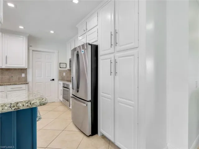 Kitchen featuring light stone counters, white cabinets, stainless steel appliances, light tile patterned flooring, and decorative backsplash