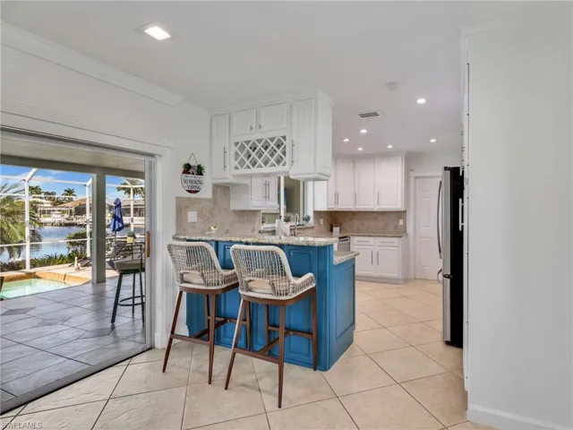Kitchen featuring white cabinets, a breakfast bar area, blue cabinetry, light stone counters, and freestanding refrigerator
