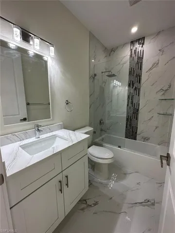 Bathroom with vanity, a combined bath / shower with marble appearance, and light marble finish flooring