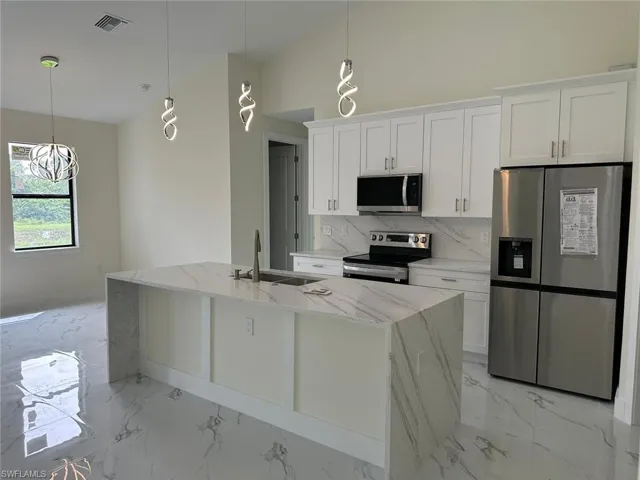 Kitchen featuring stainless steel appliances, light stone counters, white cabinets, backsplash, and vaulted ceiling