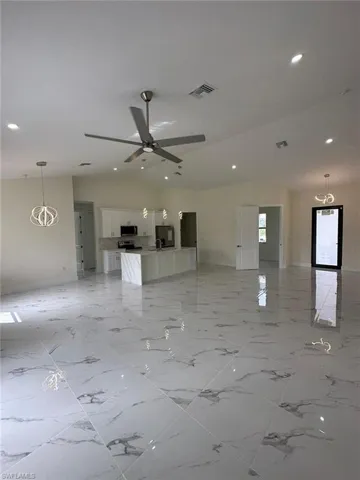 Unfurnished living room with vaulted ceiling, a ceiling fan, and suspended lighting