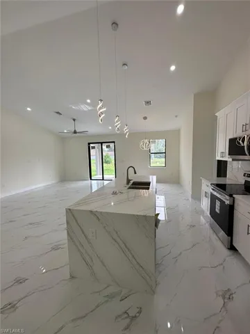 Kitchen with decorative light fixtures, stainless steel appliances, open floor plan, and white cabinets