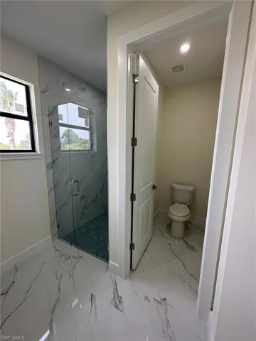 Bathroom with a marble finish shower, light marble finish flooring, and recessed lighting