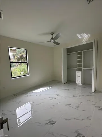 Unfurnished bedroom with a closet, light marble finish flooring, and a ceiling fan