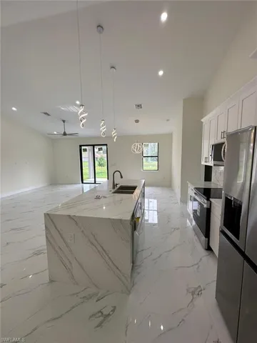 Kitchen with pendant lighting, stainless steel appliances, open floor plan, light stone countertops, and an island with sink