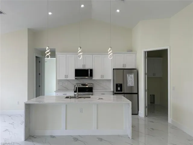 Kitchen featuring light stone countertops, stainless steel appliances, white cabinets, hanging light fixtures, and a center island with sink