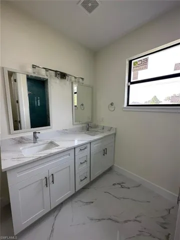 Bathroom with double vanity, a shower, and light marble finish floors