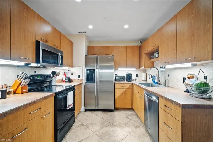 Kitchen featuring light tile patterned floors, backsplash, stainless steel appliances, and sink