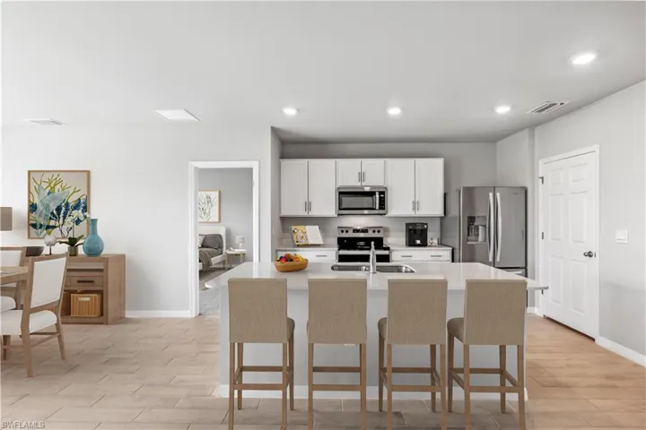 Virtually Staged-Kitchen with a breakfast bar area, a kitchen island with sink, stainless steel appliances, white cabinetry, and recessed lighting