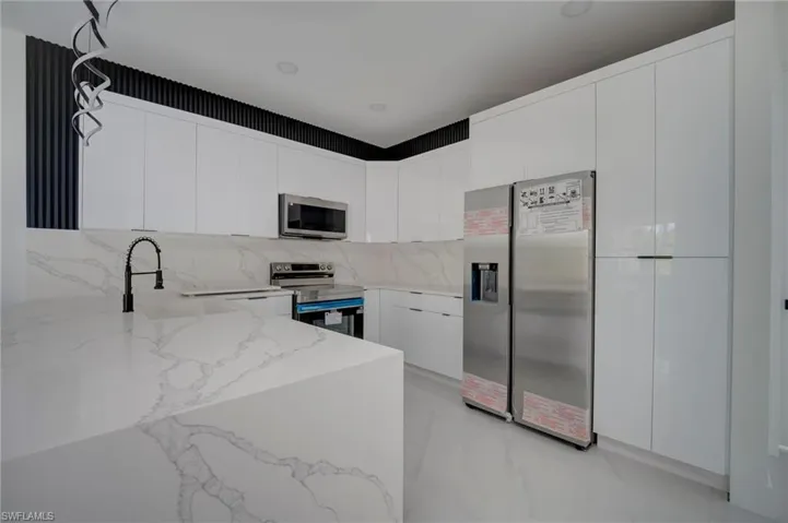 Kitchen featuring modern cabinets, stainless steel appliances, white cabinetry, light stone counters, and a peninsula