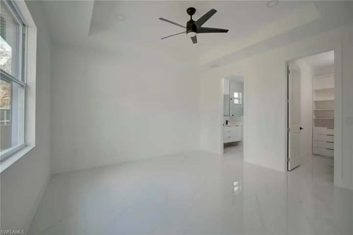 Unfurnished bedroom with a raised ceiling, a spacious closet, multiple windows, light marble finish floors, and a ceiling fan