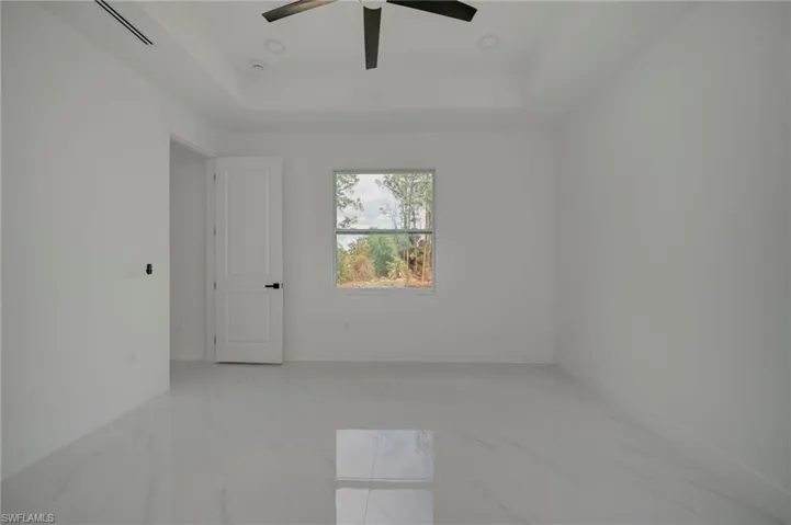 Empty room with light marble finish flooring, a ceiling fan, and a raised ceiling