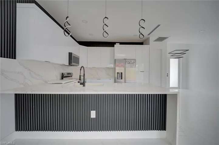 Kitchen featuring light stone countertops, a peninsula, modern cabinets, stainless steel appliances, and white cabinets