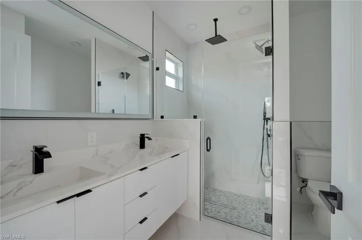 Full bathroom with double vanity, a marble finish shower, and light marble finish floors