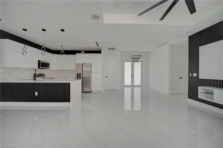 Kitchen featuring white cabinets, stainless steel appliances, modern cabinets, decorative light fixtures, and light stone counters