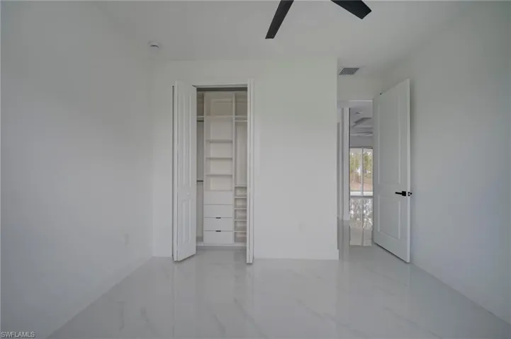 Unfurnished bedroom featuring light marble finish floors, ceiling fan, and a closet