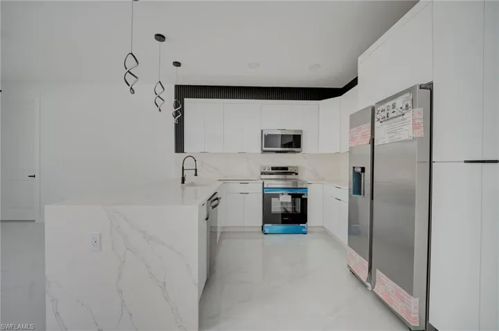 Kitchen featuring light stone countertops, decorative light fixtures, a peninsula, stainless steel appliances, and white cabinetry