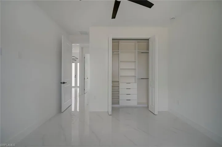 Unfurnished bedroom featuring light marble finish flooring, a ceiling fan, and a closet