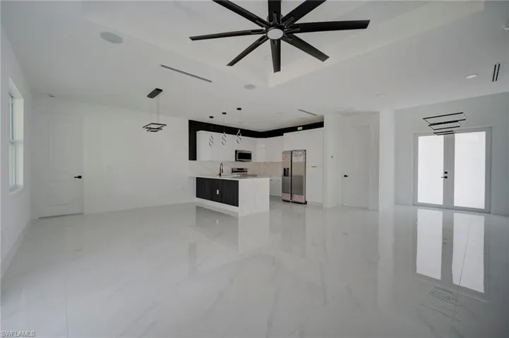 Unfurnished living room featuring a ceiling fan, a raised ceiling, and light marble finish floors