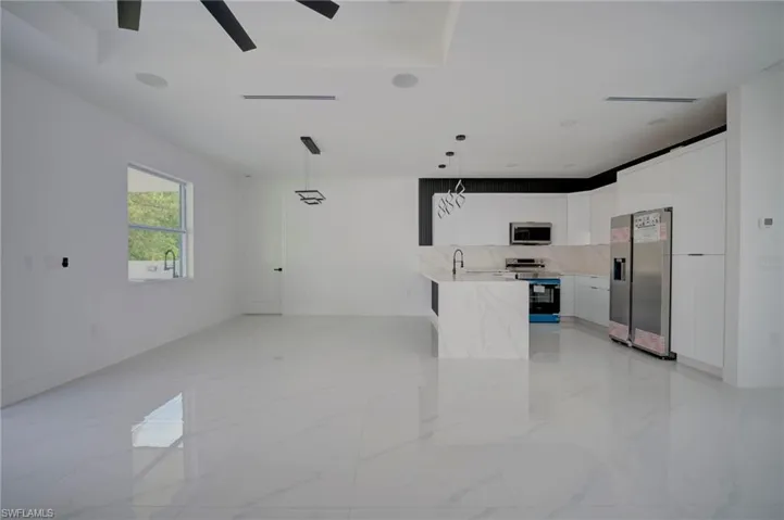 Kitchen with white cabinets, decorative light fixtures, stainless steel appliances, light stone countertops, and backsplash