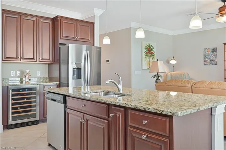 Kitchen with stainless steel appliances, crown molding, wine cooler, light stone counters, and decorative light fixtures