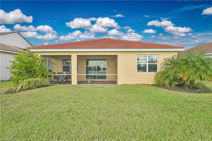 Rear view of house featuring stucco siding, a yard, and a tiled roof