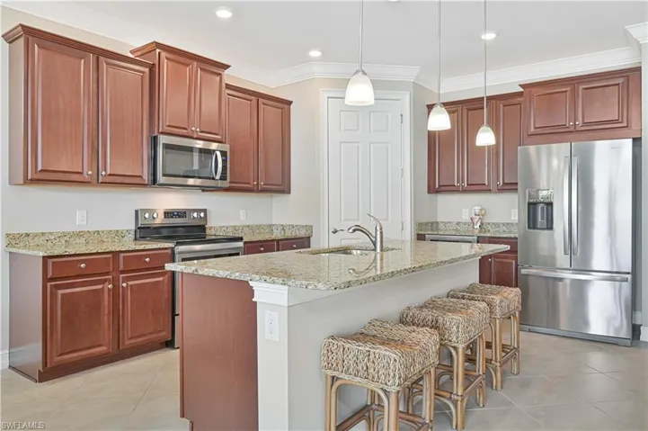 Kitchen featuring stainless steel appliances, crown molding, light stone counters, a breakfast bar area, and decorative light fixtures