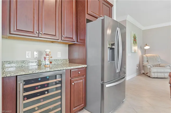 Kitchen with stainless steel fridge with ice dispenser, ornamental molding, light stone counters, beverage cooler, and light tile patterned flooring