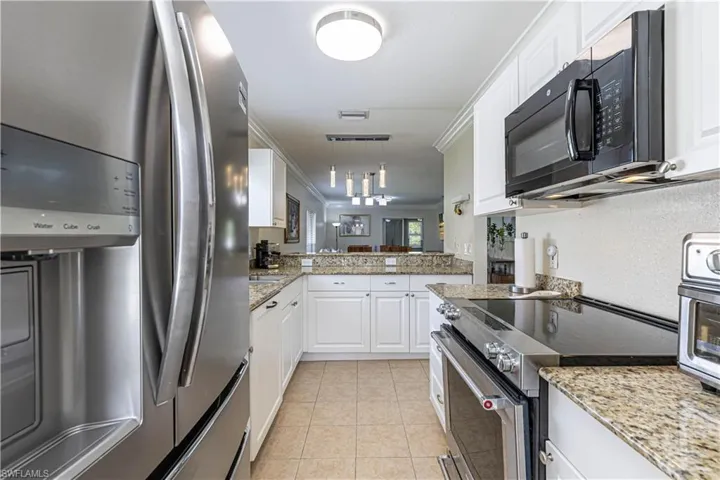 Kitchen with stainless steel appliances, light tile patterned flooring, white cabinets, pendant lighting, and light stone counters