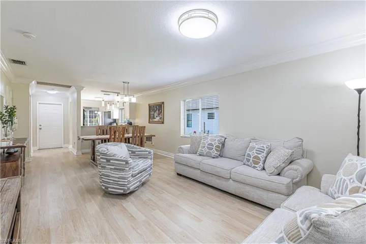 Living area with ornamental molding, light wood-style floors, a chandelier, and ornate columns