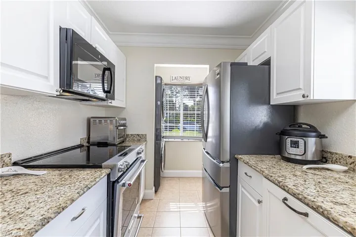 Kitchen featuring stainless steel appliances, white cabinets, light tile patterned flooring, light stone countertops, and ornamental molding