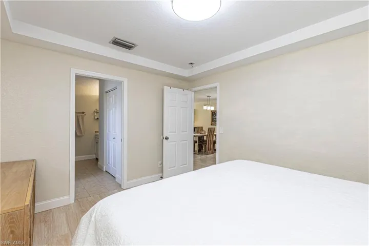 Bedroom featuring a raised ceiling, light wood-style flooring, and connected bathroom