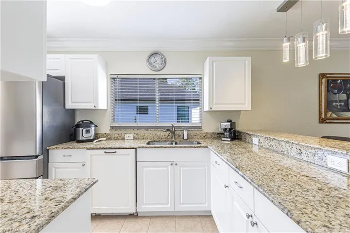 Kitchen featuring freestanding refrigerator, ornamental molding, white cabinetry, hanging light fixtures, and light stone countertops