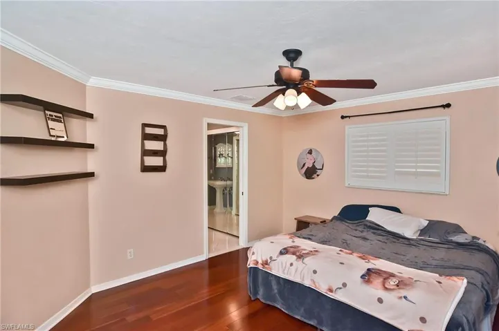 Bedroom featuring dark wood-type flooring, a ceiling fan, ornamental molding, and connected bathroom
