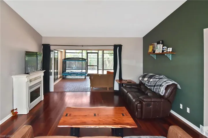 Living room featuring dark wood-style floors, vaulted ceiling, and a glass covered fireplace