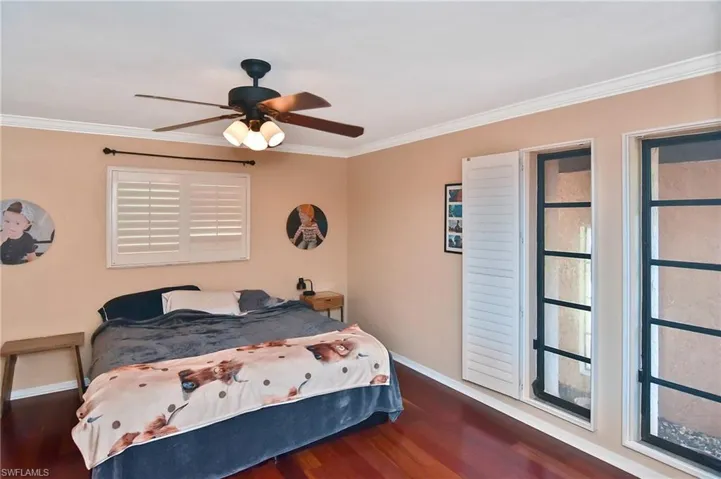 Bedroom featuring ceiling fan, dark wood-style flooring, crown molding, and multiple windows