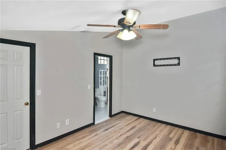 Unfurnished bedroom with light wood-style floors, ensuite bathroom, and ceiling fan