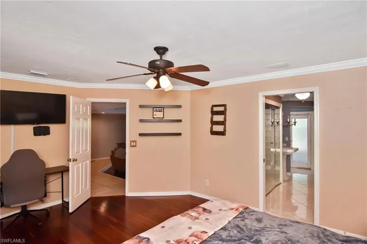 Bedroom featuring a ceiling fan, connected bathroom, an office area, ornamental molding, and wood finished floors