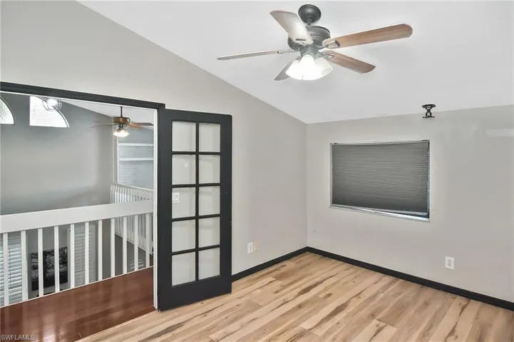 Empty room with ceiling fan, light wood-type flooring, and lofted ceiling
