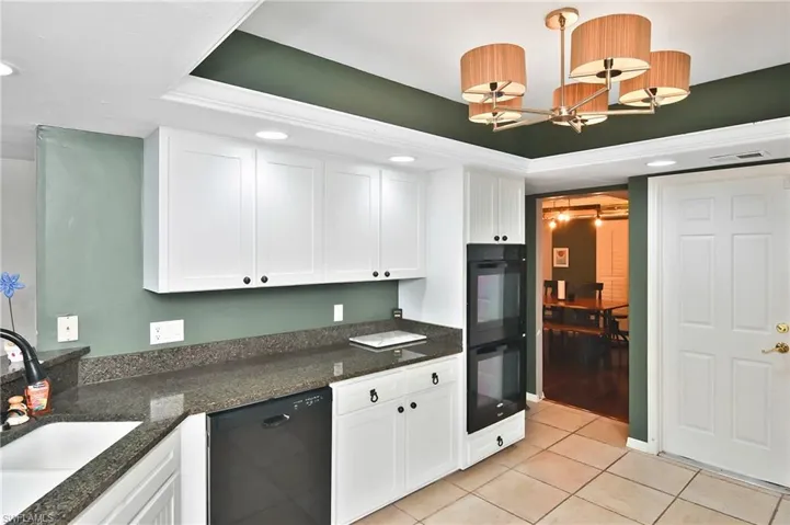 Kitchen featuring white cabinetry, black appliances, dark stone counters, a tray ceiling, and a chandelier